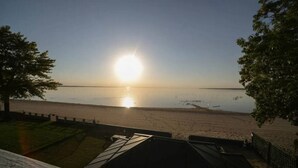 Blick auf einen Strand bei klar blauem Himmel, während die Sonne über dem Wasser untergeht oder aufgeht.