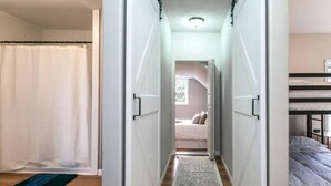Un couloir étroit avec un rideau de douche, un tapis, un lit avec un matelas et un lit superposé.