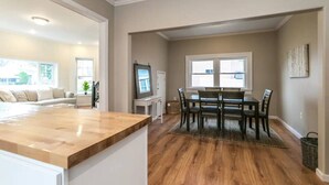 Une cuisine moderne avec un plan de travail en bois, un coin repas avec une table et des chaises, et un salon avec un canapé et un téléviseur.