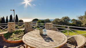 Una mesa de madera al aire libre con sillas de mimbre, un pilar de piedra y vista al mar.
