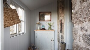 A rustic interior with a wooden cabinet, a woven basket, a pair of boots, and a stone wall. - Butterwell Cottage at Collihole (Newton Abbot)
