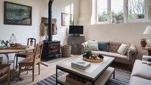 A cozy living room with a fireplace, a sofa, a coffee table, and a television. - Butterwell Cottage at Collihole (Newton Abbot)
