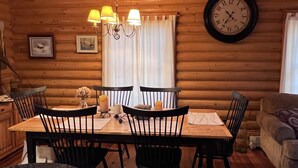 A wooden cabin interior with a dining table, four chairs, a chandelier, a clock, and a couch. - Cozy cabin near Conway Lake and North Conway (Center Conway)