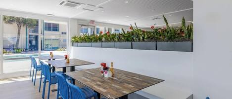 A modern indoor dining area with blue chairs, wooden tables, and a plant wall.