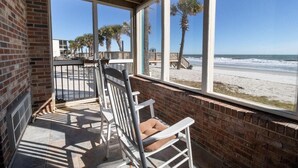 Ein Balkon am Strand mit Blick auf das Meer, ein weißer Schaukelstuhl und eine Backsteinmauer.