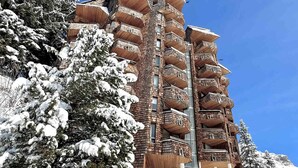 Ein mehrstöckiges Gebäude mit hölzernen Balkonen, umgeben von schneebedeckten Bäumen.