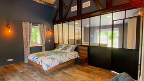 Un dormitorio con cama, una silla, un ventanal y un espejo.