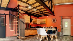 Una cocina moderna con una escalera de madera, un comedor con sillas y un reloj en la pared.
