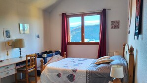 A bedroom with a bed, a desk, a chair, a window with curtains, and a view of the outdoors.