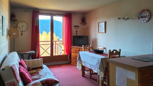 A cozy room with a sofa, a dining table, and a TV. There's a window with a view of mountains.