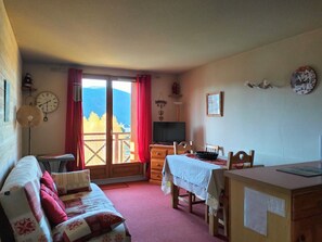 Habitació acollidora amb un sofà, una taula de menjador i una televisió. Hi ha una finestra amb vista a les muntanyes.