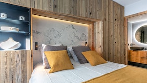 A modern bedroom with a wooden headboard, a bed with white linens, and a built-in shelf with decorative items.