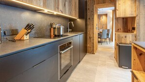 A modern kitchen with wooden accents, a built-in oven, and a dining area visible through an open doorway.
