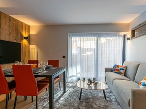 A modern living room with a dining area, featuring a sofa, a coffee table, and a TV mounted on a wooden wall.