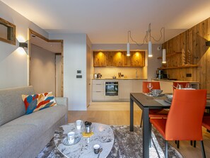 A modern kitchen with wooden cabinets, a dining area with a table and chairs, and a living area with a sofa and coffee table.