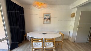 Een eetgedeelte met een ronde tafel, vier houten stoelen, een hanglamp en een lijst met een afbeelding aan de muur.