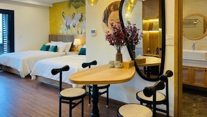 A hotel room with a bed, a dining table with chairs, a mirror, and a vase with flowers. - FLC Sea Tower - Quynhon Homes (Quy Nhon Nam)