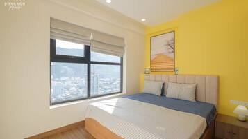A bedroom with a large window, a bed, a nightstand, and a wall-mounted lamp.