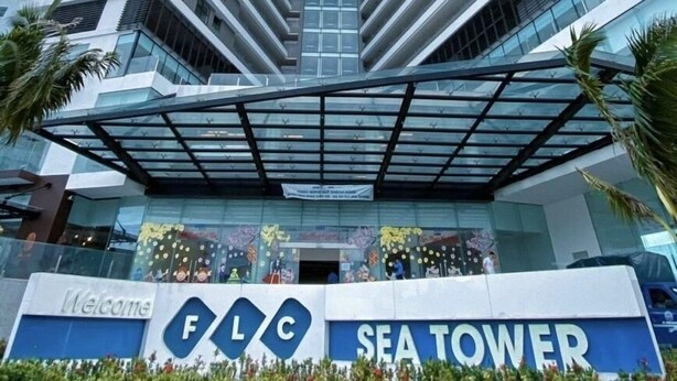 A modern high-rise building with a distinctive angular design, featuring a prominent entrance with a glass canopy and a sign reading "FLG SEA TOWER". - FLC Sea Tower - Quynhon Homes (Quy Nhon Nam)