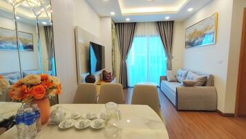 A modern living room with a sofa, a dining table with water bottles and teapots, and a TV.