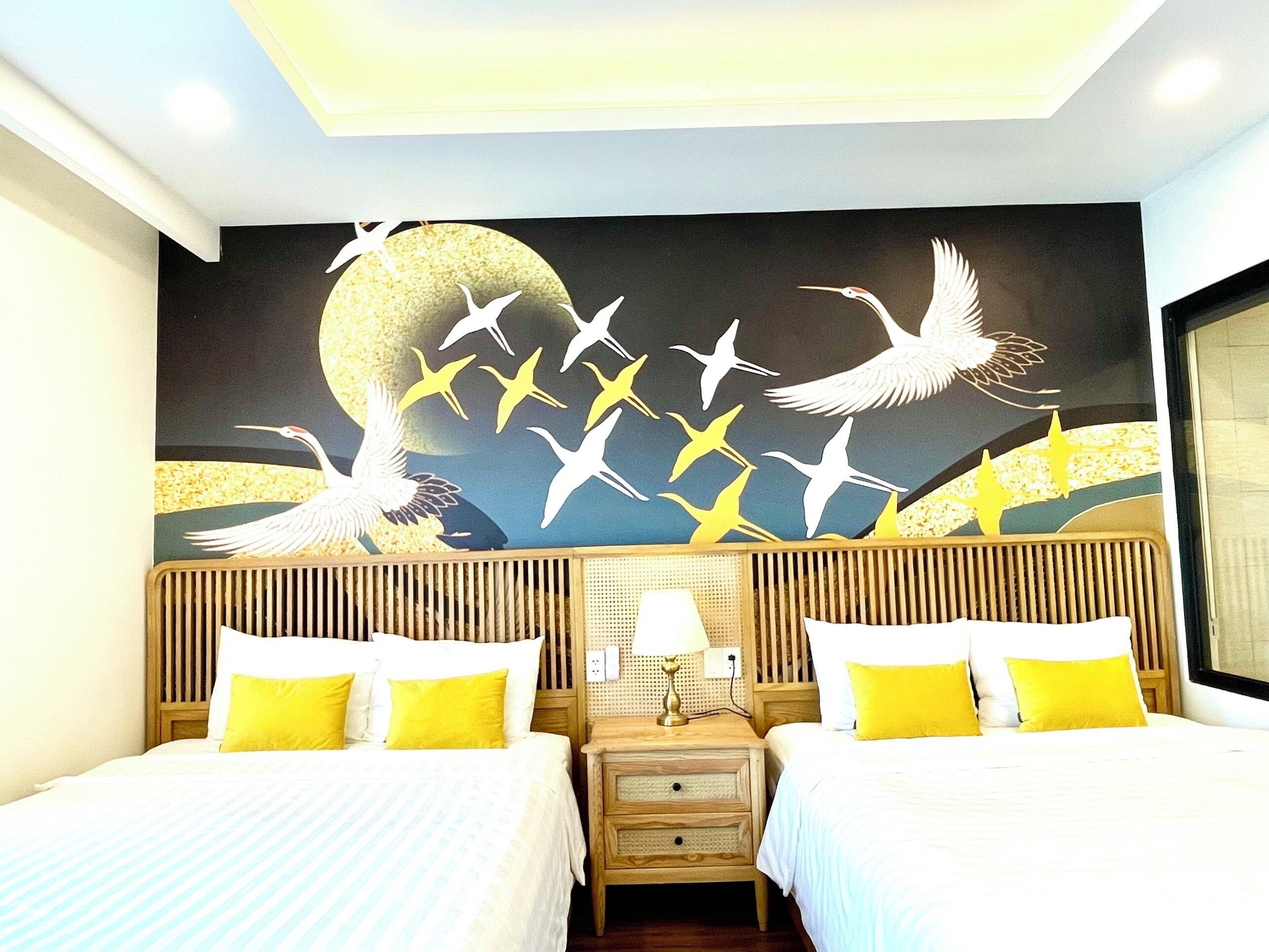 A hotel room with two beds, a nightstand, and a wall mural of birds flying.
