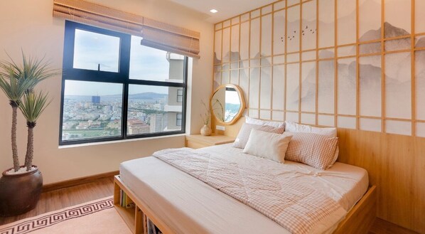 A bedroom with a large window, a bed, a bedside table, a mirror, and a decorative wall panel. - FLC Sea Tower - Quynhon Homes (Quy Nhon Nam)