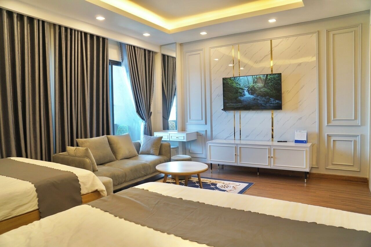 A modern hotel room with a large bed, a sofa, a small round table, and a TV mounted on the wall.