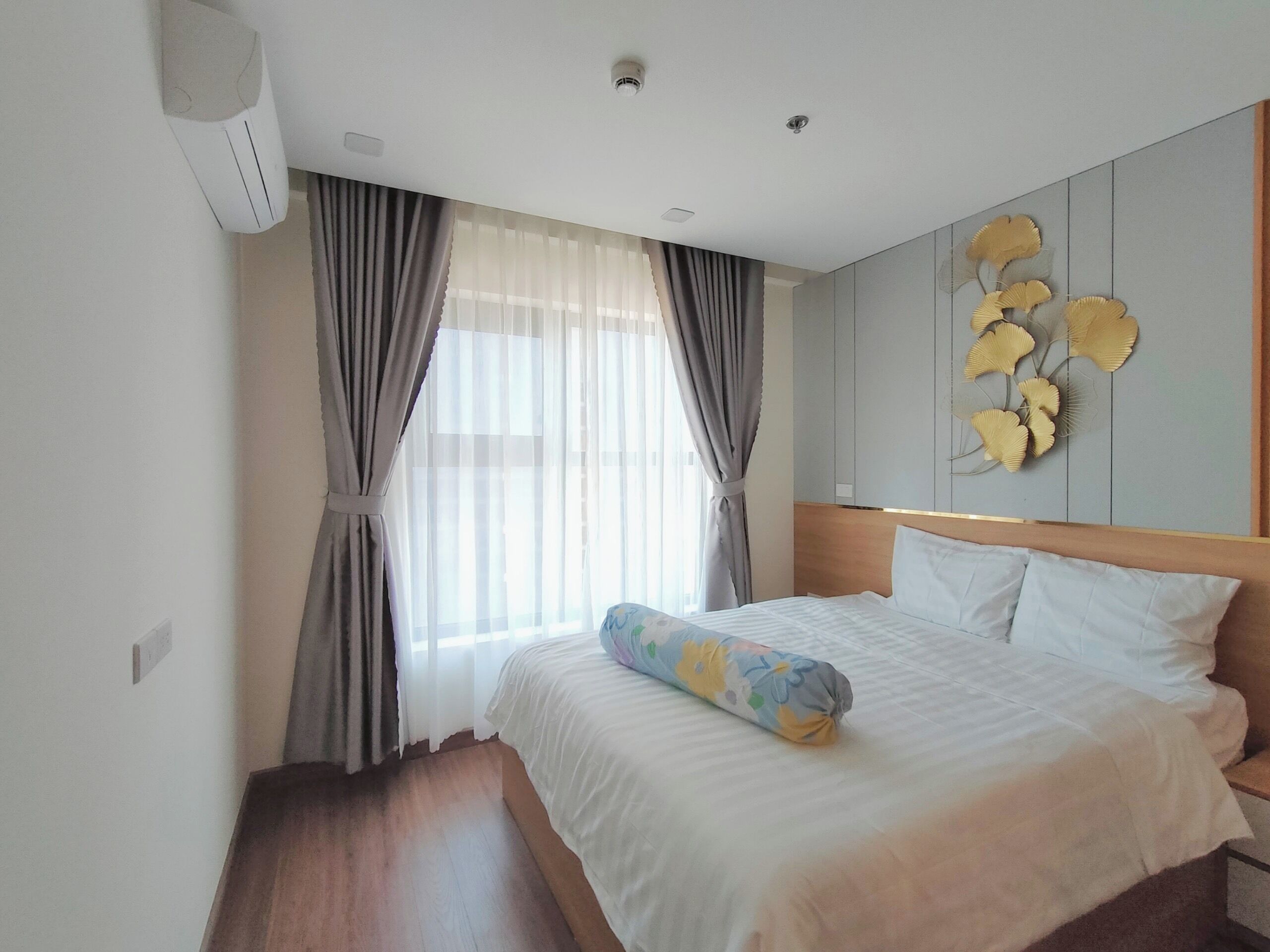 Habitación de hotel con cama, cortinas, aire acondicionado de pared y un adorno en la pared.
