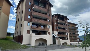 A multi-story residential building with balconies, a covered entrance, and a parking area. - 6-Person Apartment at Foot of Slopes, Balcony, Equipped Kitchen (Morillon 1100)