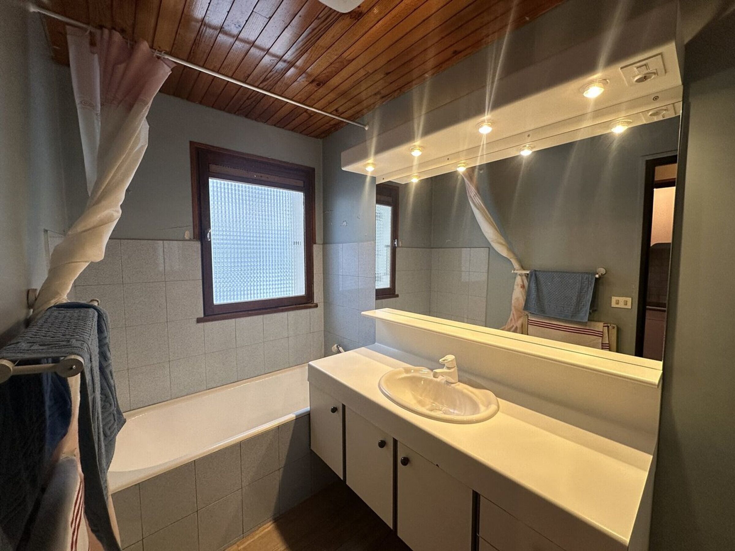 Ein Badezimmer mit Badewanne, Waschbecken, Spiegel und einem Fenster mit Vorhang.