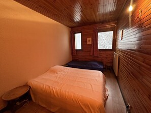 A small, cozy room with wooden walls and a single bed. There is a small table and a window with curtains. - 100m² Duplex for 9 near lifts in village center (Les Carroz d'Arâches)