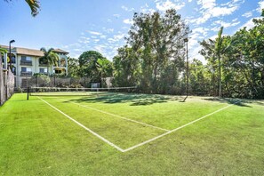 Un court de tennis avec un filet, entouré d’arbres et avec un bâtiment en arrière-plan.