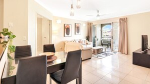 A spacious living area with a dining table, chairs, a sofa, and a TV. There is a balcony with a view. - Cairns One Resort Style Living- Luxury Resort Apartment | 9 Pools | Near CBD & Esplanade (Westcourt)