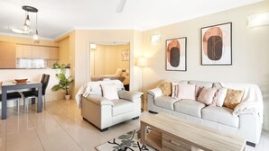 A modern living room with a sofa, a coffee table, and a dining area with chairs and a table. - Cairns One Resort Style Living- Luxury Resort Apartment | 9 Pools | Near CBD & Esplanade (Westcourt)