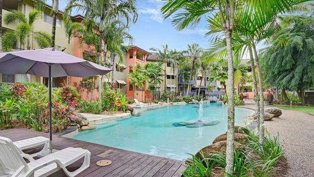 A pool area with lounge chairs, a water feature, and tropical plants. - Cairns One Resort Style Living- Luxury Resort Apartment | 9 Pools | Near CBD & Esplanade (Westcourt)