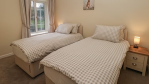 Un dormitori amb dos llits, una finestra amb cortines, un quadre a la paret i una tauleta de nit amb una làmpada.