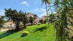A residential area with well-maintained lawns, palm trees, and buildings with red-tiled roofs. - Palmira 1Bed/1Bath at the Tennis Village, Palmas del Mar (Humacao)