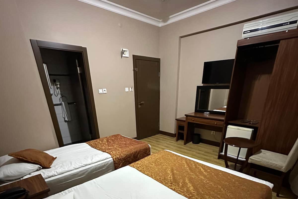 Habitación de hotel con dos camas, un escritorio, una silla, un televisor y un equipo de aire acondicionado.