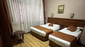 Habitación de hotel con dos camas, suelo de madera, una mesita y un ventanal con cortinas.