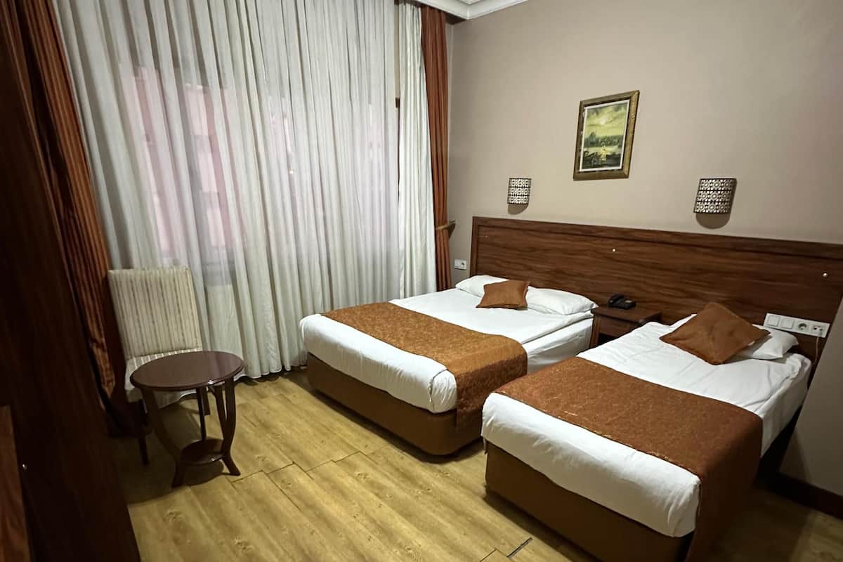 Habitación de hotel con dos camas, suelo de madera, una mesita y un ventanal con cortinas.