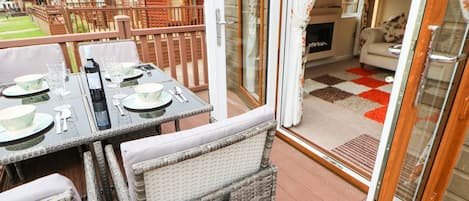 A patio with wicker furniture, a table set for dining, and a view of wooden cabins in the background.