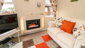 A living room with a fireplace, a sofa, a TV, and a glass coffee table. - 10 Poppy Lodge (Richmond)