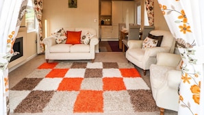A cozy living room with a sofa, two armchairs, a patterned rug, and a kitchen in the background. - 10 Poppy Lodge (Richmond)