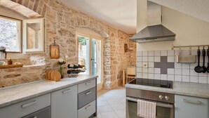 Une cuisine aux murs en pierre, dotée d’une cuisinière moderne et d’un pare-feu en carreaux.