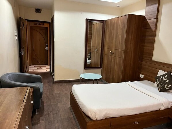 A bedroom with a bed, a desk, a chair, a small round table, and a wardrobe. - Hotel Ken (Ranchi)