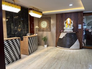 A reception area with a black marble wall, a clock, and a statue. - Hotel Ken (Ranchi)