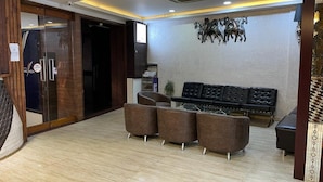 Et reception område med moderne design, med en receptionsdisk, et siddeområde med tre sofaer, en vægmonteret hestesulptur og en stor skærm.
