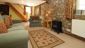 Una sala de estar acogedora con una pared de piedra, una chimenea, un sofá, un sillón y una escalera.