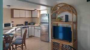 Una cocina compacta con armarios blancos, un refrigerador, un microondas, una estufa y un comedor con mesa y sillas.