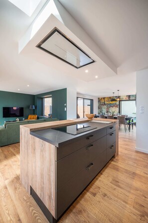 A modern kitchen with a central island, wooden flooring, and a skylight.